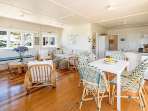 A spacious living area with a dining table, wicker chairs, a sofa, and a kitchen area.