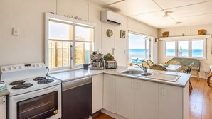 A kitchen with a stove, dishwasher, and a view of the ocean. - Beachfront Bliss - Opposite Onetangi Beach (Waiheke Island)
