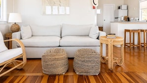 A modern living room with a sofa, two woven ottomans, a lamp, and a map on the wall. - Beachfront Bliss - Opposite Onetangi Beach (Waiheke Island)