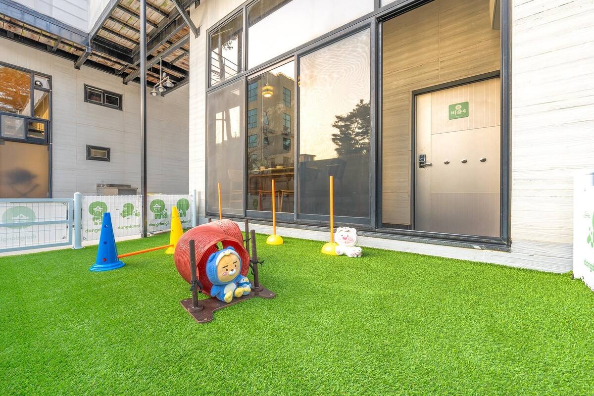 A children's play area with artificial grass, a toy train, and a small white dog.