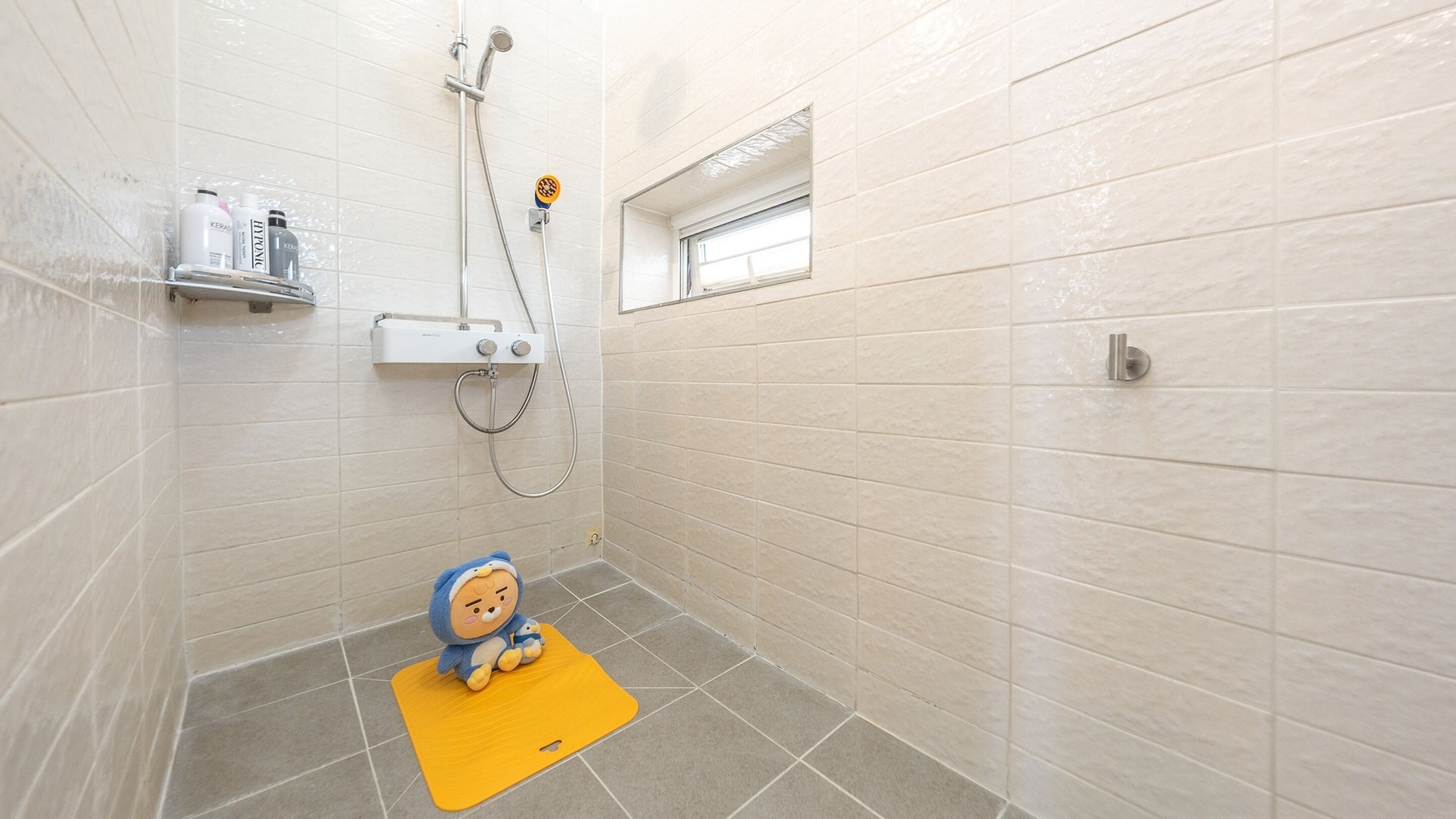 A bathroom with a shower, a small window, and a shelf with toiletries.