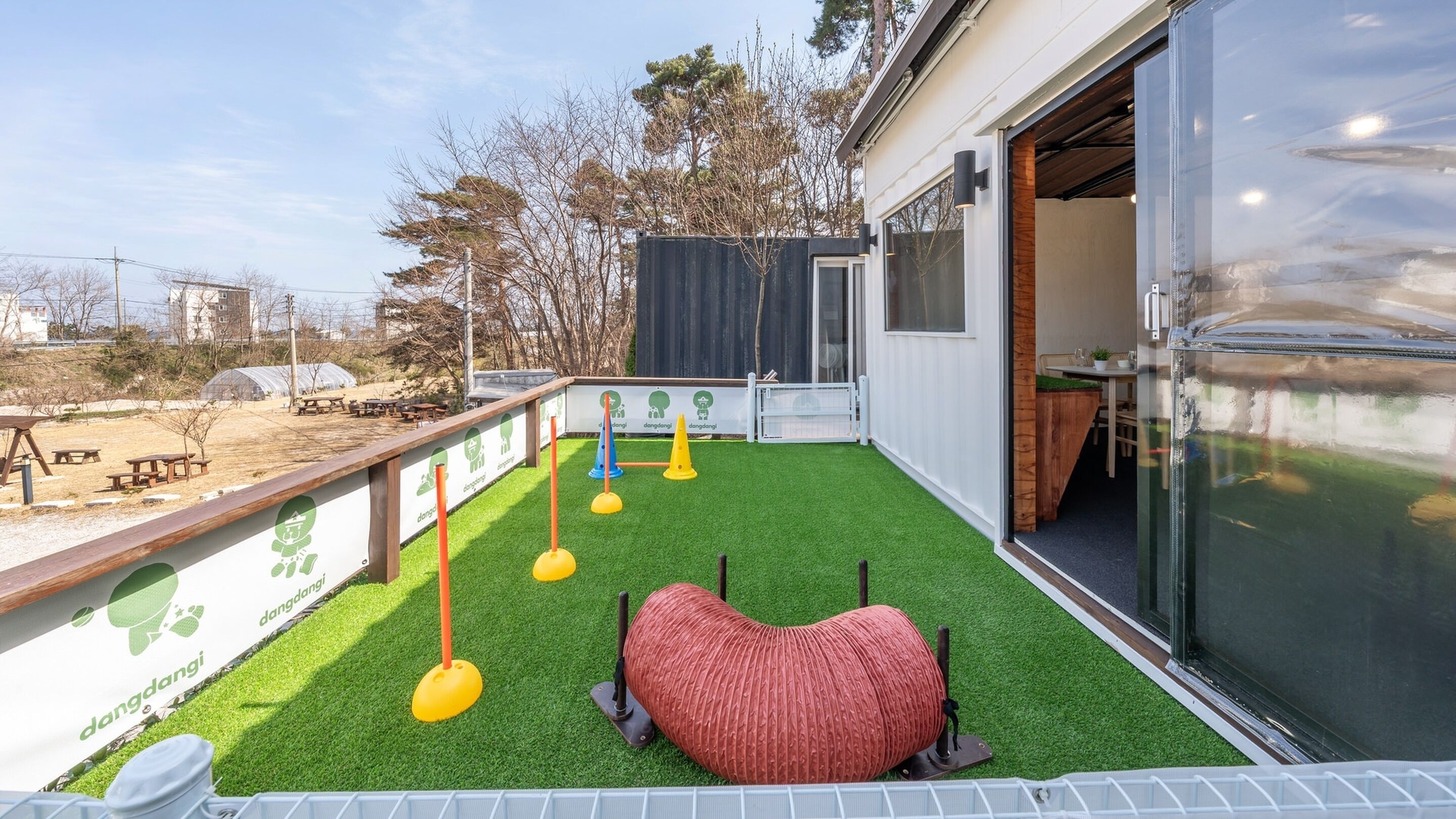 Un espace extérieur moderne avec un gazon synthétique, un pouf en forme de cœur et des cônes de couleur vive.