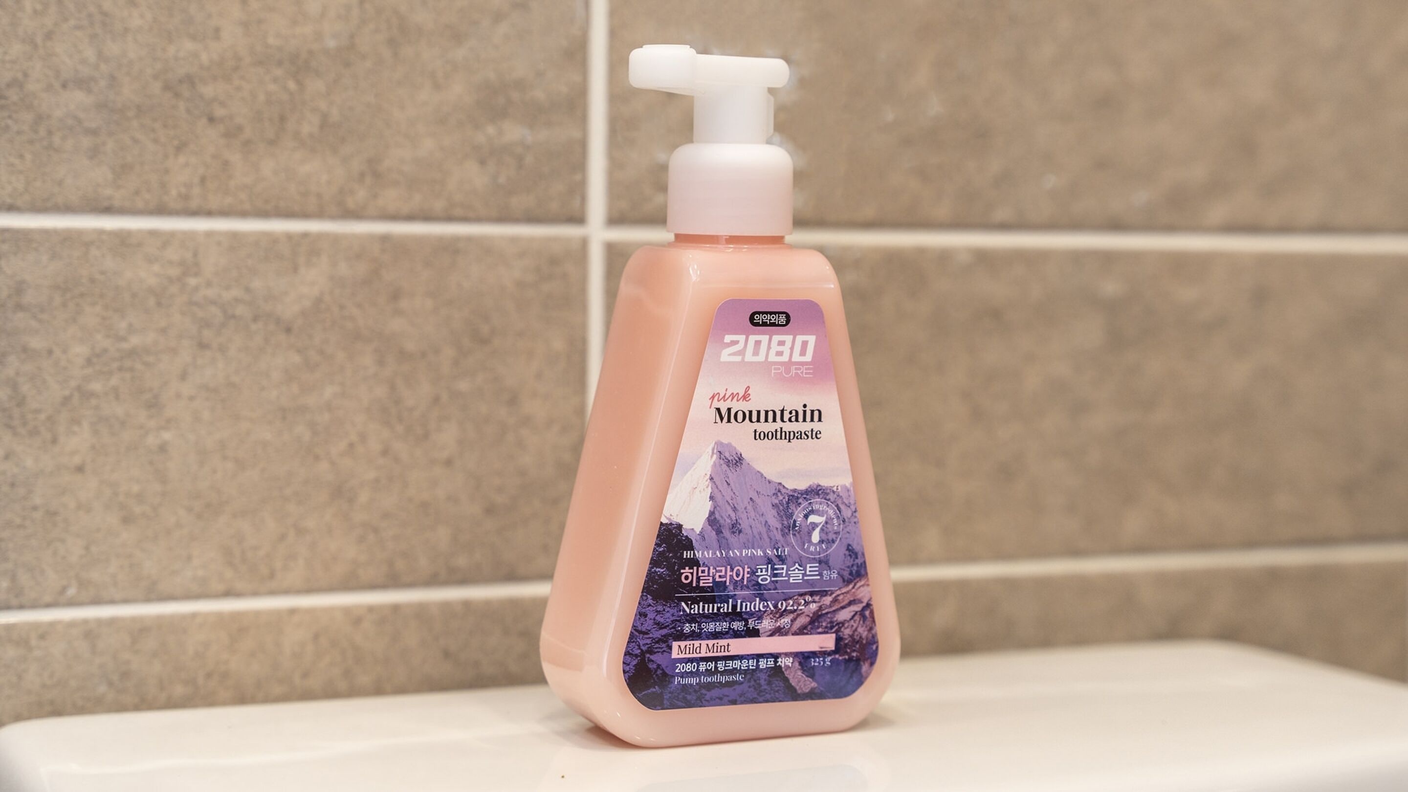 A pink pump bottle of Mountain toothpaste with a mountain image on the label, placed on a white surface against a tiled wall.