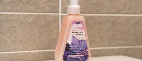A pink pump bottle of Mountain toothpaste with a mountain image on the label, placed on a white surface against a tiled wall.