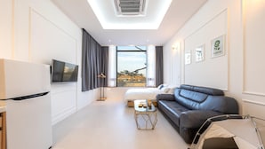 A modern hotel room with a flat-screen TV, a sofa, a small table, and a bed. - Gangneung Dangdangi Dog Pension Blue (Gangneung)