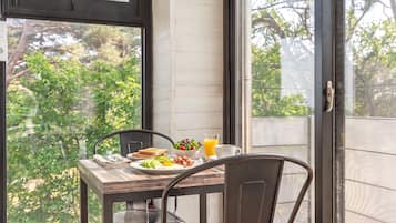 A dining table with breakfast items, a chair, and a view of trees through a window.