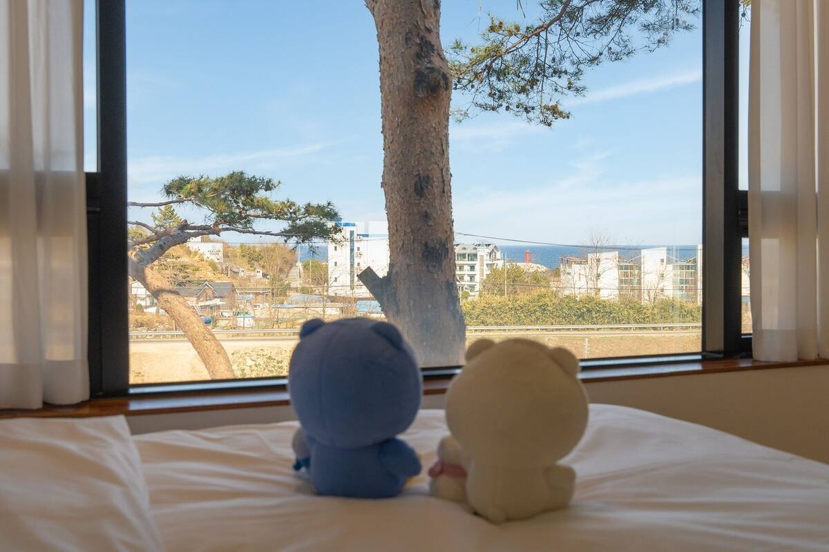 A bedroom with a large window, a bed, and two teddy bears.