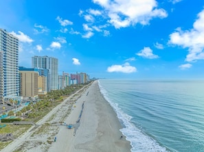 A coastal cityscape with high-rise buildings, a sandy beach, and a clear blue sky. - Camelot By The Sea 1614 (Myrtle Beach)