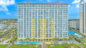 A high-rise hotel with multiple balconies, a swimming pool, and a view of the surrounding area. - Camelot By The Sea 1614 (Myrtle Beach)