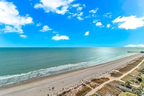 Uma praia costeira com um cais, areal e céu claro.