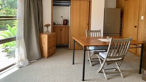 Ein kleines Zimmer mit einem Holztisch, zwei Stühlen, einem Holzschrank, einem Kühlschrank und einem Fenster mit Vorhängen.