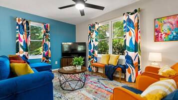 A living room with a blue sofa, orange armchairs, a TV, and colorful curtains.