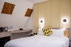 Habitación de hotel con cama, mesita de noche y escritorio con teléfono, cafetera y botellas de agua.