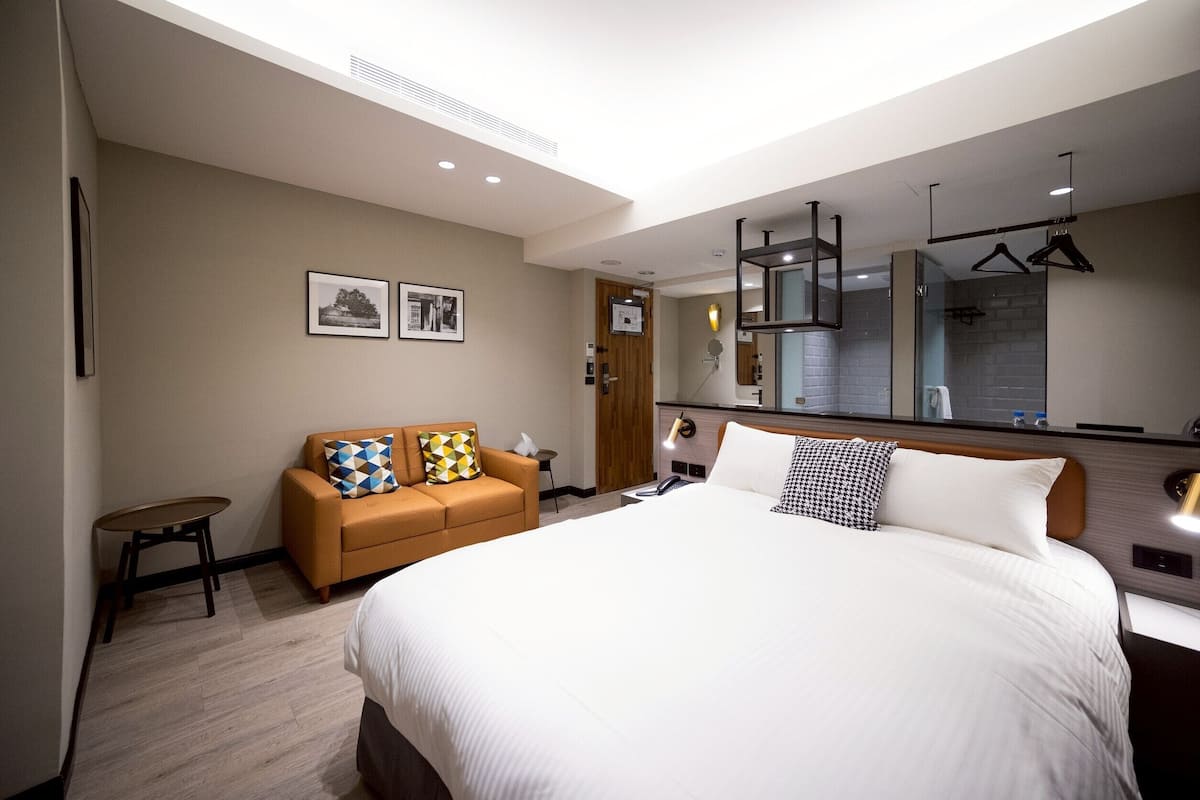 A modern hotel room with a large bed, a sofa, a small table, and a mirror.