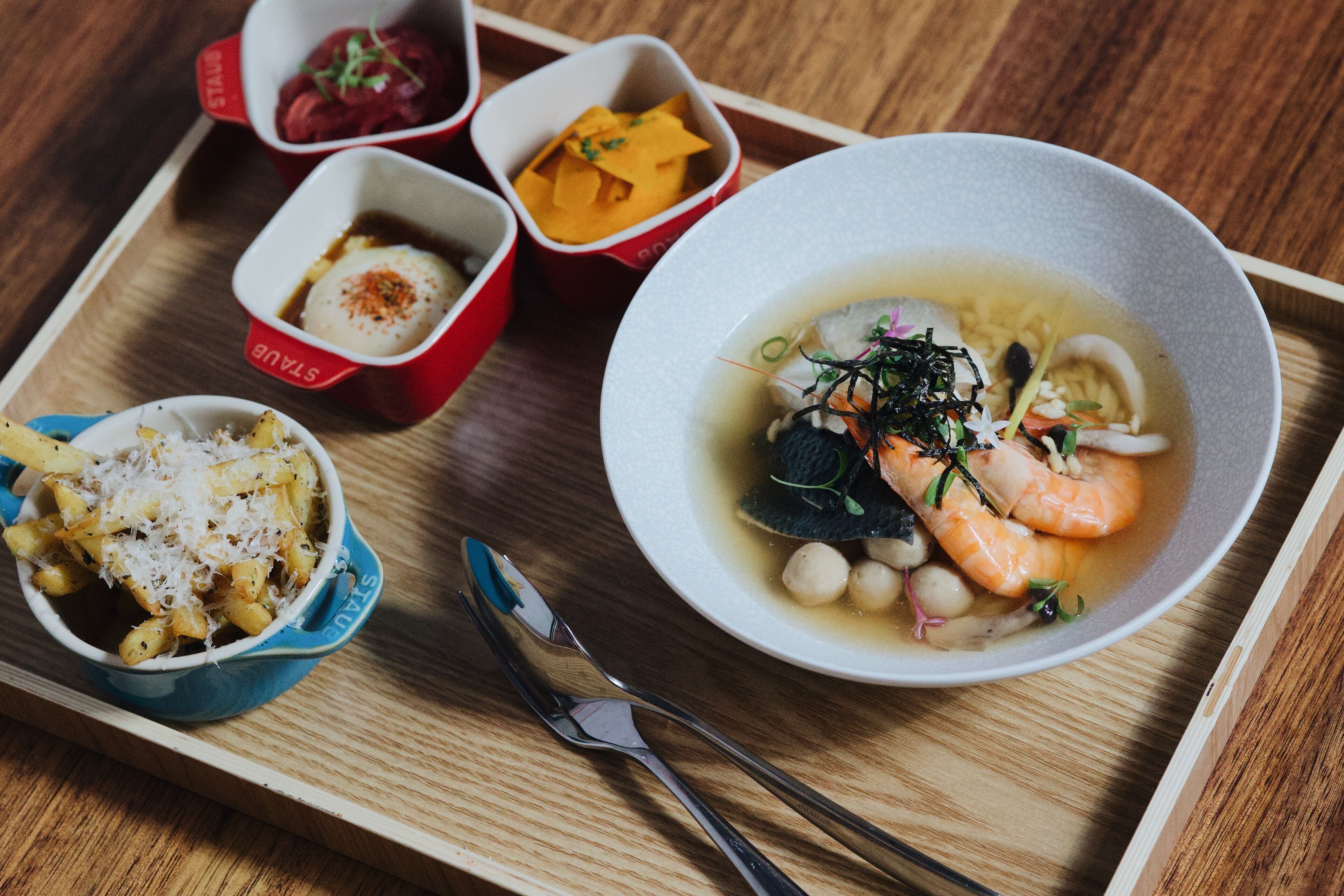 A tray with a bowl of soup, a bowl of pasta, and two small bowls of side dishes.