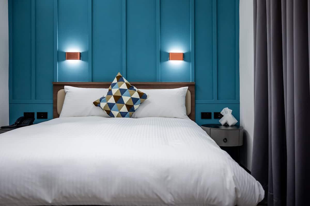 A hotel room with a large bed, two bedside tables, a nightstand, and a blue accent wall with lighting.