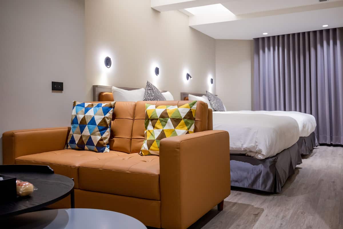 A modern hotel room with a sofa, a round table, and a large bed with multiple pillows.