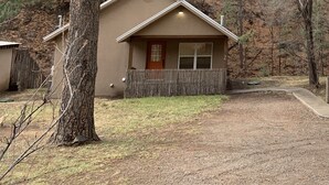 Une petite cabane à un seul étage, dotée d’un porche à l’avant et entourée d’arbres.