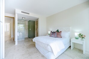 Quarto moderno com uma cama grande, mesa de cabeceira e área de chuveiro.