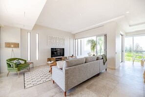 A modern living room with a large sofa, a television, and a dining area.