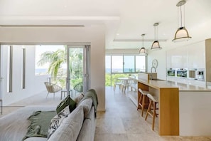 A modern kitchen with a bar area, large windows, and a view of the ocean. - The Platinum 3BR Luxe Residence in Sunshine Beach (Sunshine Beach)