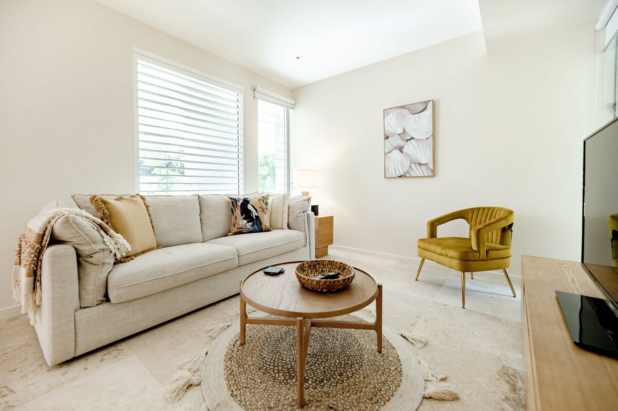 A living room with a sofa, a coffee table, a yellow chair, and a wall-mounted artwork.