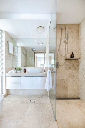 A modern bathroom with a glass shower enclosure, a white vanity with a large mirror, and a marble-tiled floor.