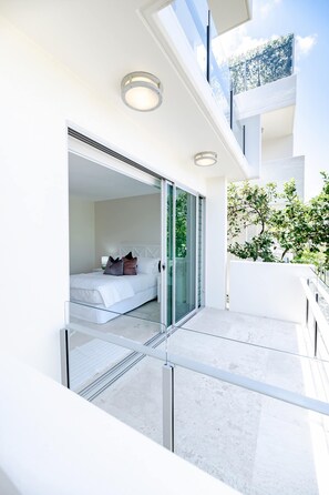 Quarto moderno com porta de vidro que dá para uma varanda, cama com almofadas e mesa de cabeceira com abajur.