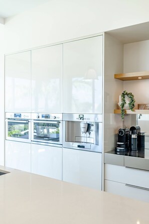Cozinha moderna com eletrodomésticos embutidos, incluindo duas fornos, uma máquina de café e um dispenser de água.