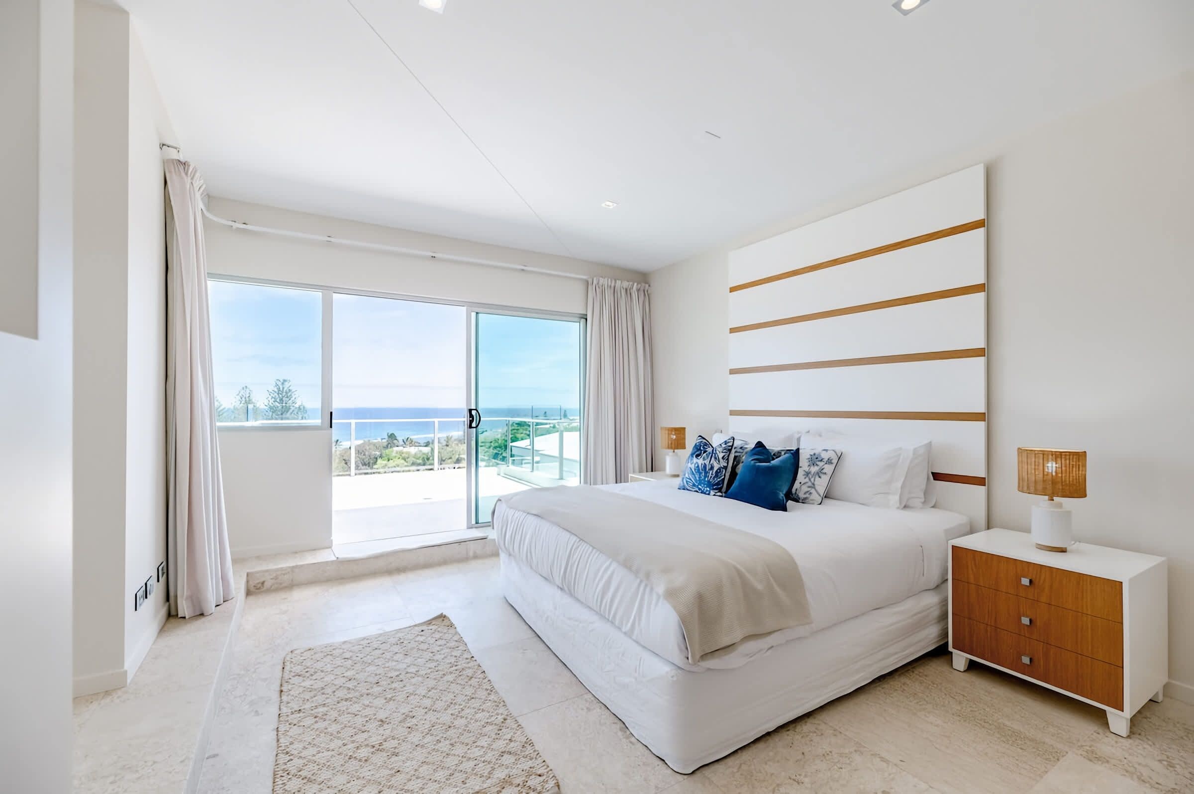 A modern bedroom with a large bed, a nightstand, and a view of the ocean.