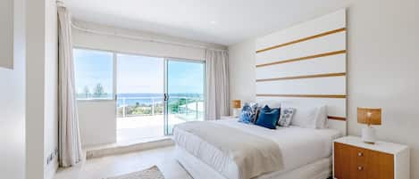 A modern bedroom with a large bed, a nightstand, and a view of the ocean.
