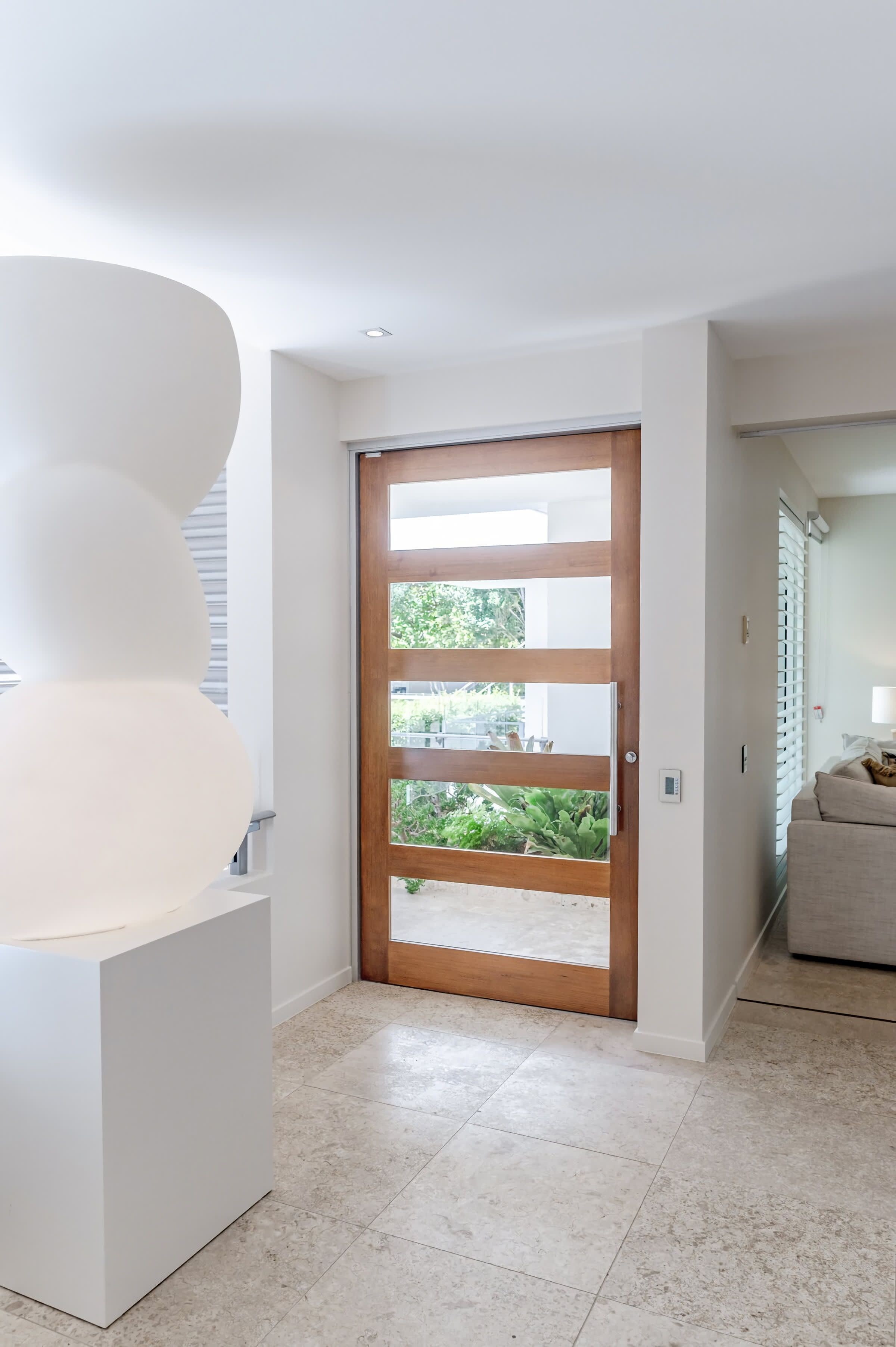 Un interior moderno con una puerta de madera, paredes blancas y suelo de baldosas.