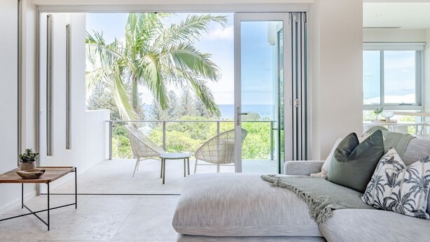 Ein modernes Schlafzimmer mit einer großen Schiebeglasdoor zum Balkon mit Blick auf Palmen und das Meer.
