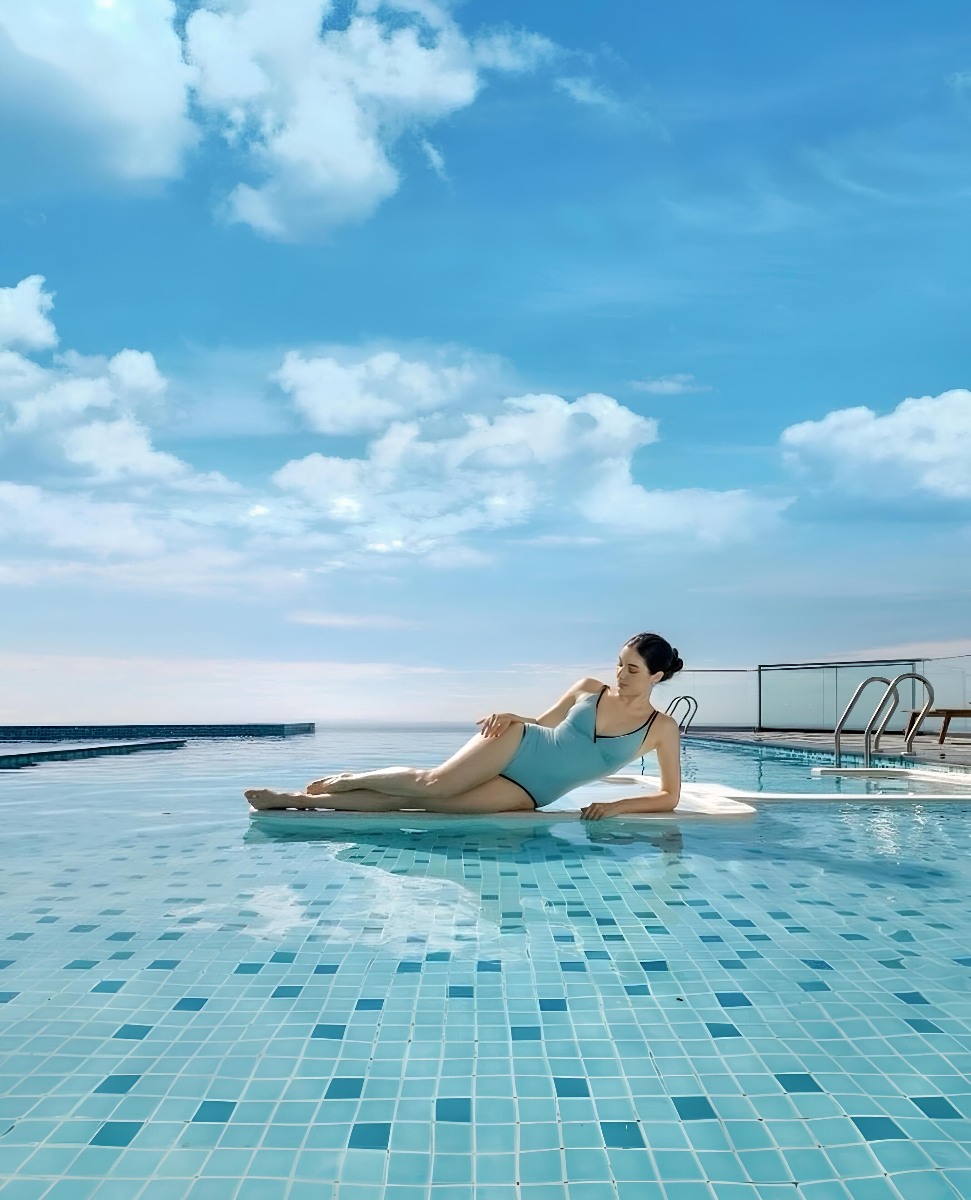 Une personne allongée au bord d’une piscine, sous un ciel bleu dégagé.