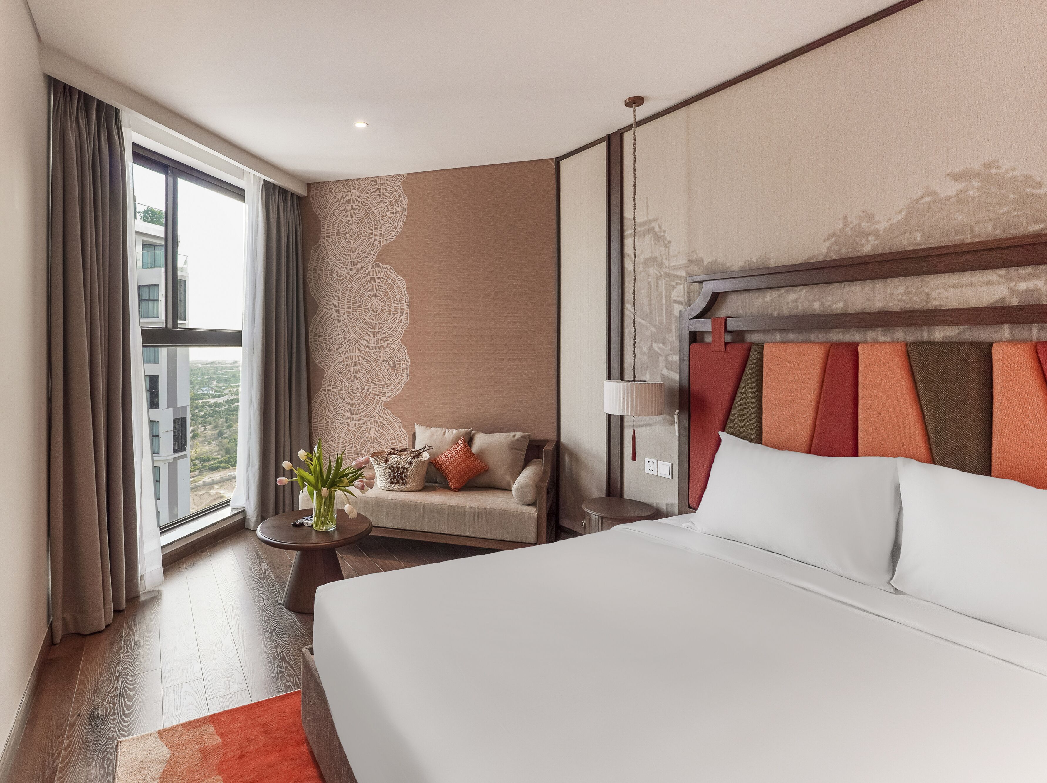 Habitación de hotel con una cama grande, un sofá, una mesita y vistas a la ciudad a través del ventanal.