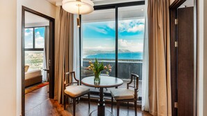 Una habitación con un ventanal grande, una mesa redonda con sillas, un jarrón con flores y vistas al mar.