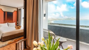 Habitación de hotel con cama, vista al mar y balcón con mesa y sillas.