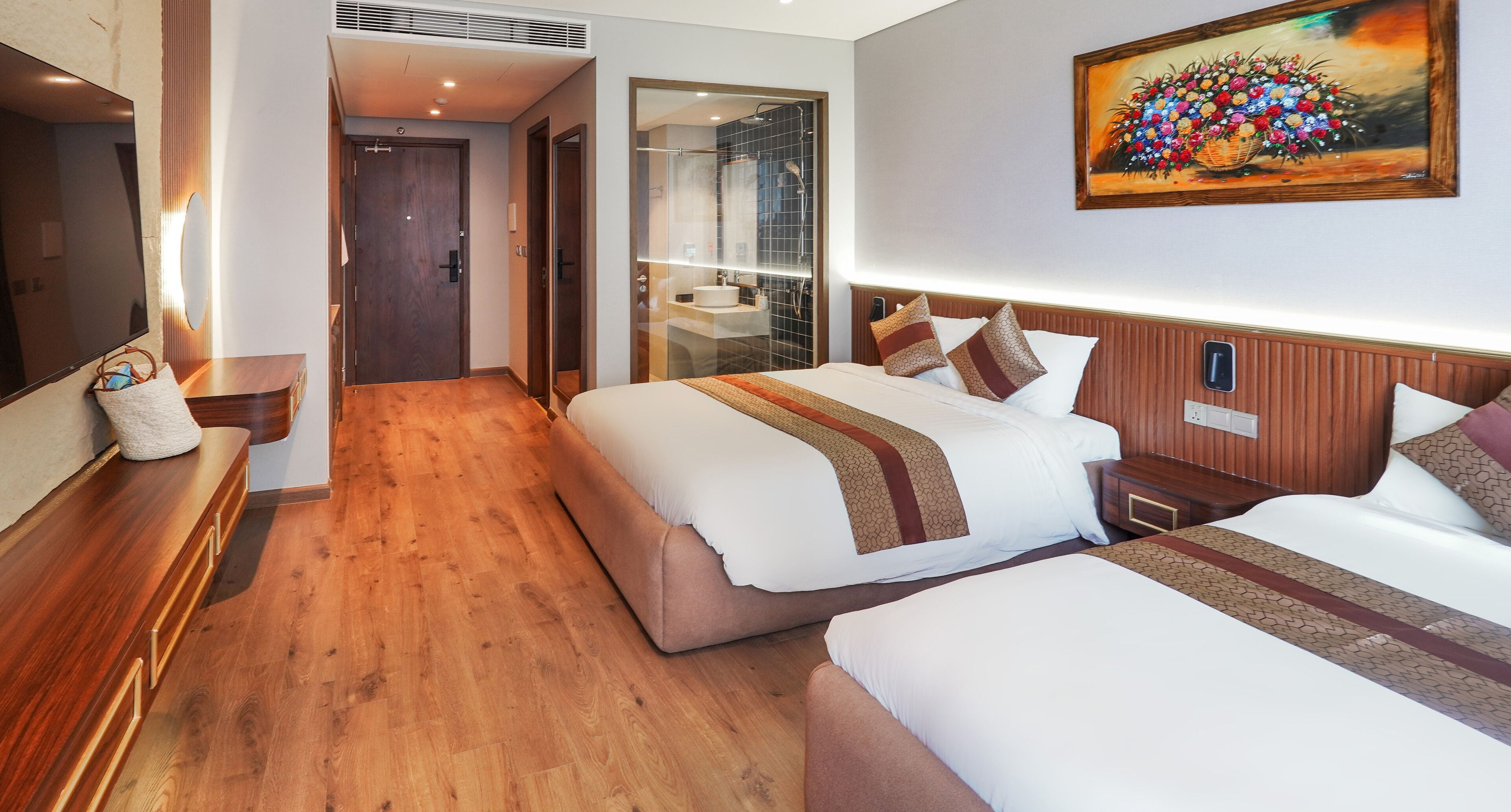 A hotel room with two beds, a large mirror, a wooden floor, and a painting on the wall.