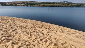 Una playa arenosa con un lago tranquilo y colinas al fondo.