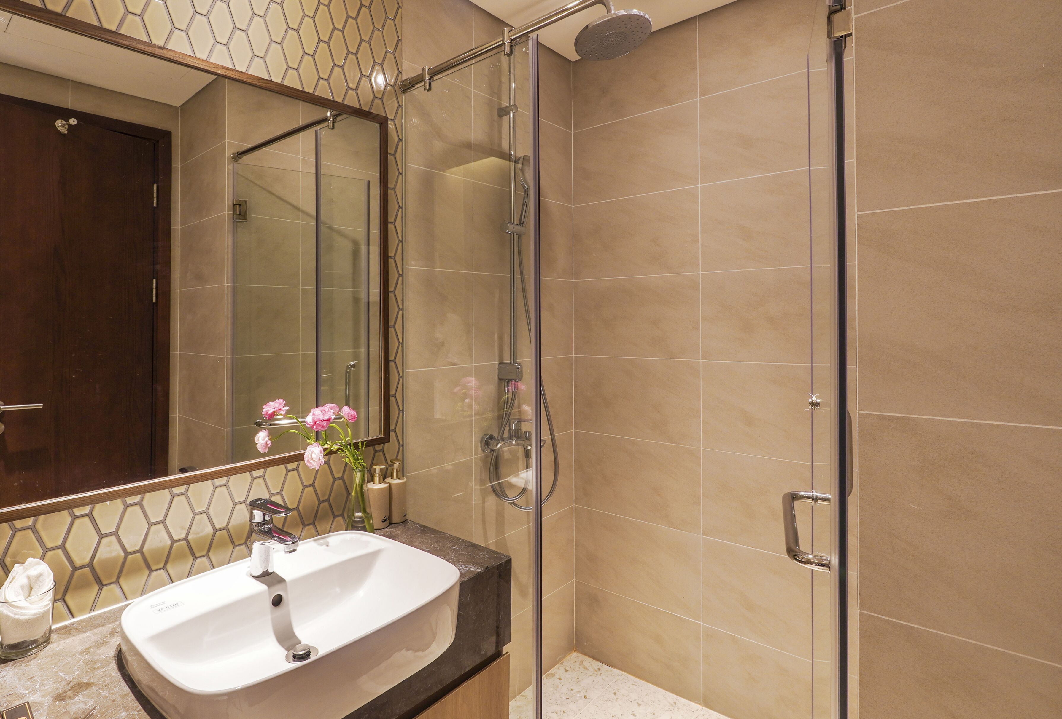 A bathroom with a glass-enclosed shower, a sink with a marble countertop, and a mirror above the sink.