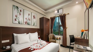 A hotel room with a large bed, a desk, a chair, a window with curtains, and artwork on the wall. - Nhan Hoa Hotel (Hanoi)