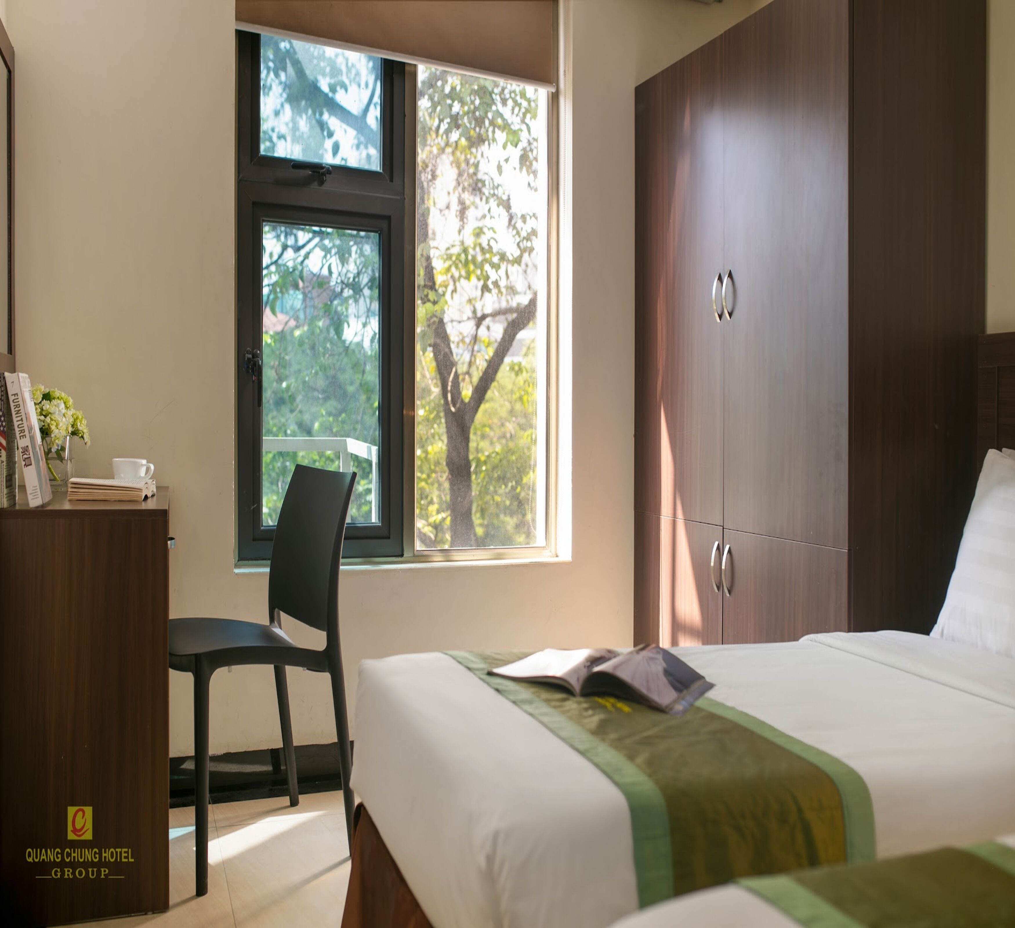 Een hotelkamer met een bed, een bureau met stoel, een raam met uitzicht op bomen, en een kledingkast.