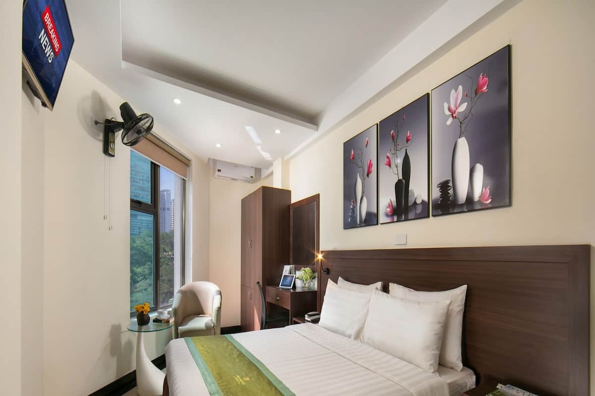 A hotel room with a large bed, a desk, a chair, and artwork on the wall.