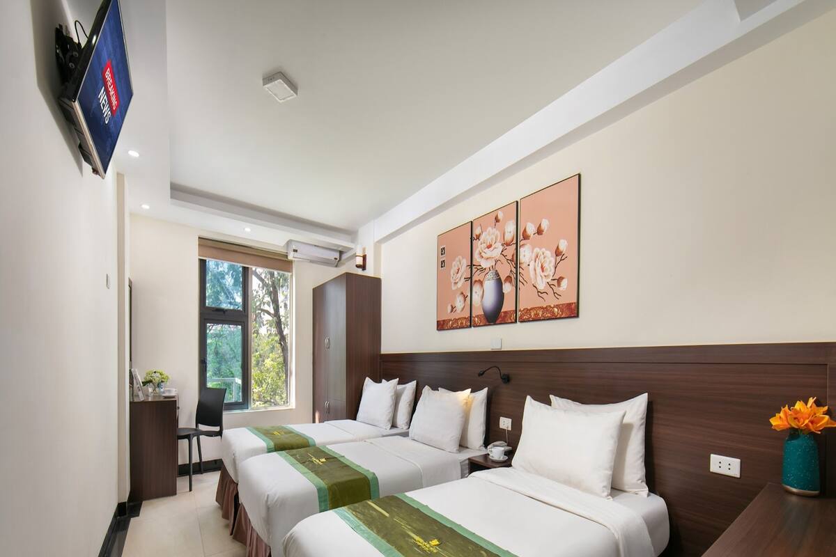 A hotel room with two beds, a desk, a TV, a window, and a painting on the wall.