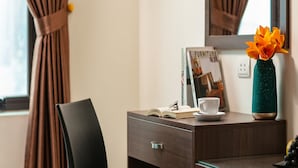 A hotel room with a wooden desk, a black chair, a white cup, a book, and a vase with flowers. - Nhan Hoa Hotel (Hanoi)
