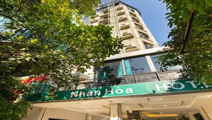 A hotel entrance with a staircase leading to the lobby, surrounded by greenery and a view of a tall building in the background. - Nhan Hoa Hotel (Hanoi)
