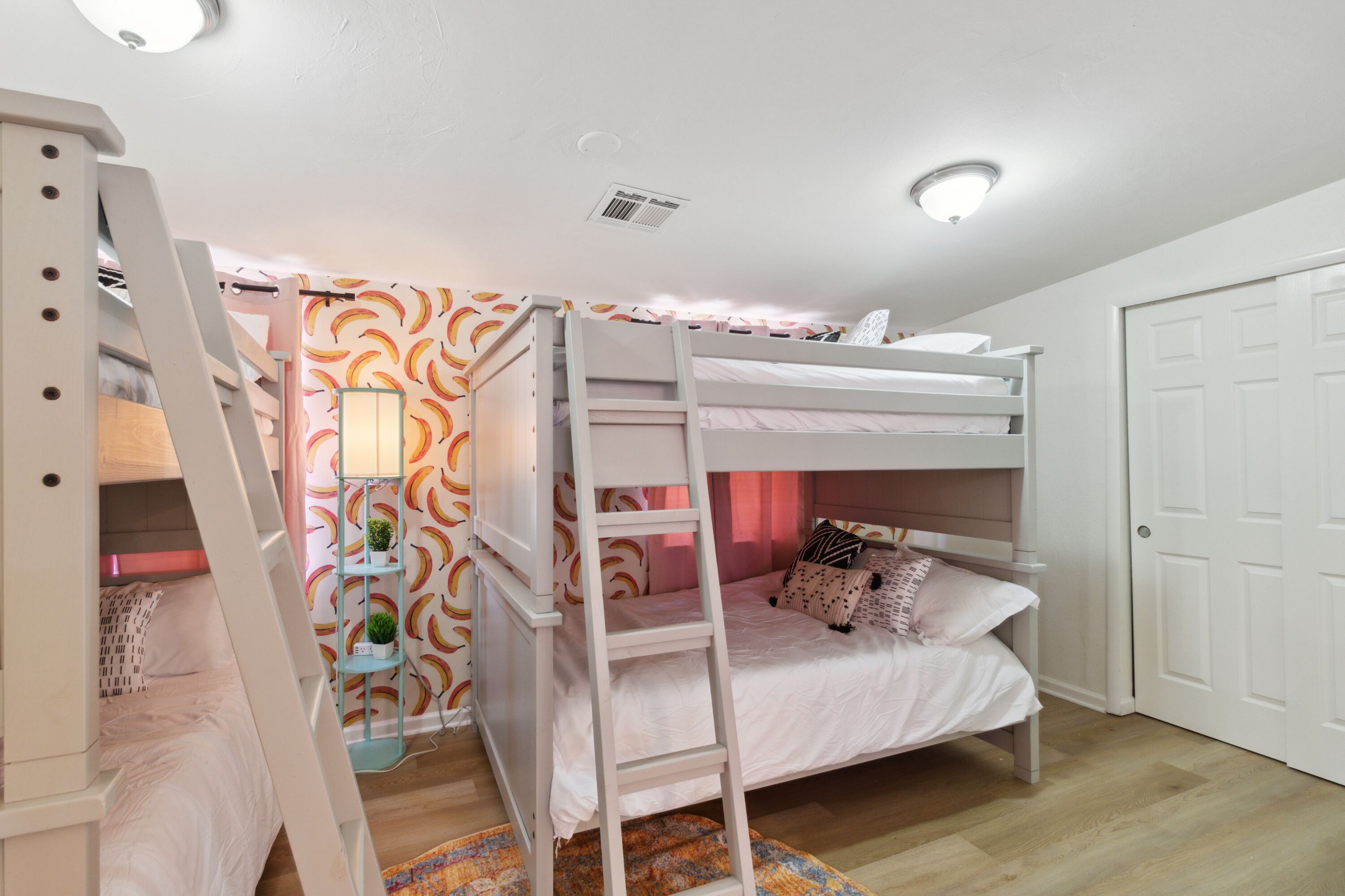 A bunk bed room with a ladder, a small shelf with a plant, and a door.