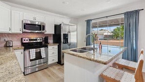 Una cocina moderna con armarios blancos, electrodomésticos de acero inoxidable, encimera de granito y ventana con cortinas azules.