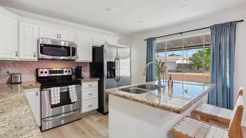 A modern kitchen with white cabinets, stainless steel appliances, a granite countertop, and a window with blue curtains.