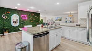 Una cocina moderna con armarios blancos, encimera de granito, electrodomésticos de acero inoxidable y una pared verde con un letrero de neón.